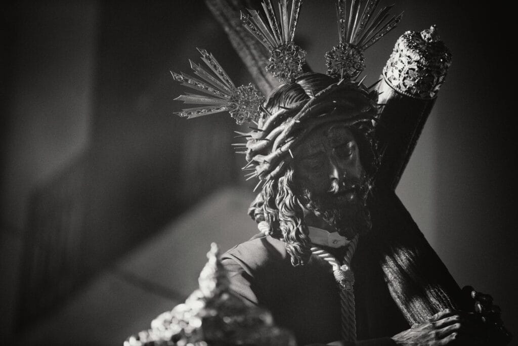 Hooded figure holding two candles in darkness